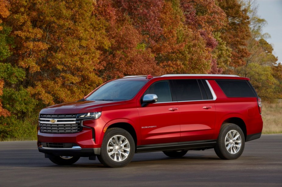 A red 2022 Chevrolet Suburban parked outdoors in front of a wooded area. 