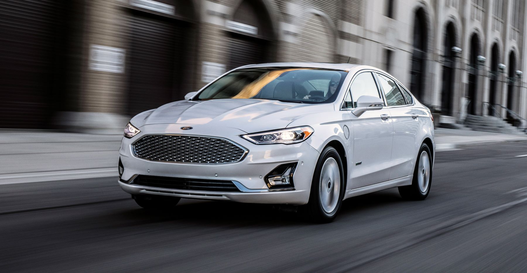 A white 2022 Ford Fusion midsize sedan model driving through a metropolitan city