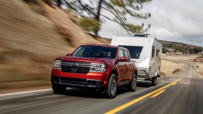 Promo shot of a red Ford Maverick towing a camper trailer up a hill.