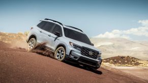 A light gray 2022 Honda Passport TrailSport adventure SUV model driving down a dirt hill, which was graded poorly by the IIHS