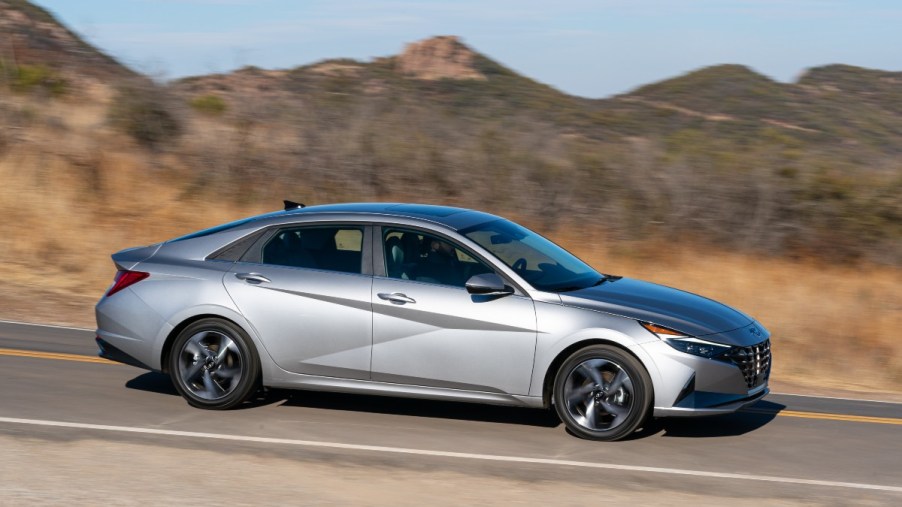 a silver 2022 hyundai elantra drives along a road with mountains in the background