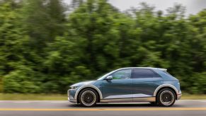 A side shot of a teal 2022 Hyundai Ioniq 5 electric SUV/EV model driving on a forest highway