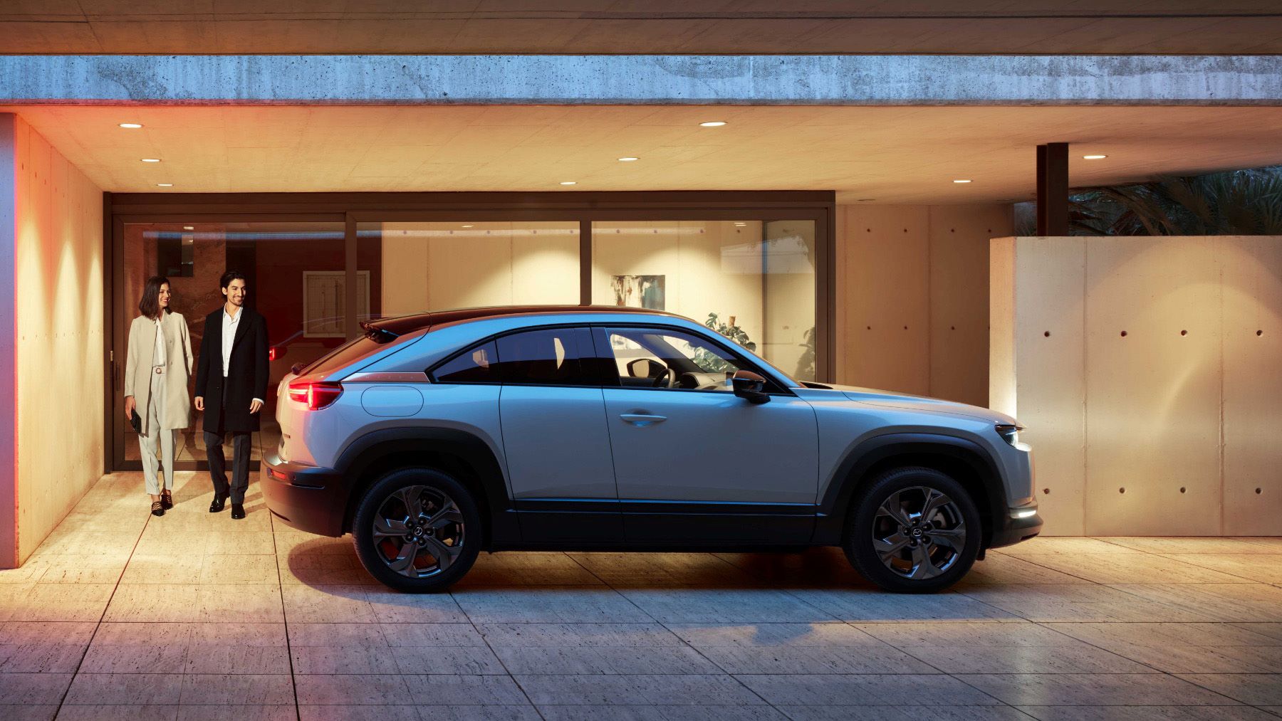 The 2022 Mazda MX-30 EV parked on a marble plaza right outside a building as a well-dressed couple approaches