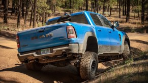 Blue Ram 1500 TRX off-roading in front of a wooded mountainside.