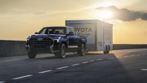 Blue Toyota Tundra pickup truck towing a Toyota Racing trailer down an empty interstate.