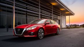 Sporty red 2022 Nissan Altima sedan parked next to a garage building at sunset