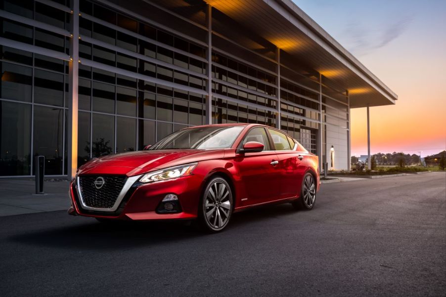 Sporty red 2022 Nissan Altima sedan parked next to a garage building at sunset