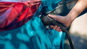 A person plugs a charging cable into the charging port of a teal 2022 Toyota Prius Prime