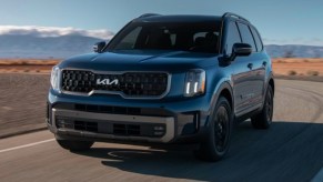 A blue 2023 Kia Telluride midsize SUV is driving on the road.