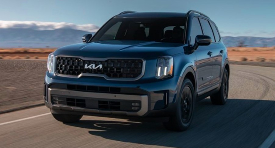 A blue 2023 Kia Telluride midsize SUV is driving on the road.