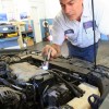 A technician visually inspects a car engine bay with a flashlight as part of an emissions test in California