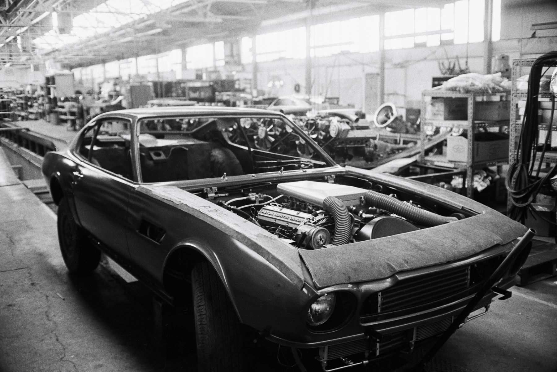 A removed hood on an Aston Martin car with engine, powertrain, and fuel injectors