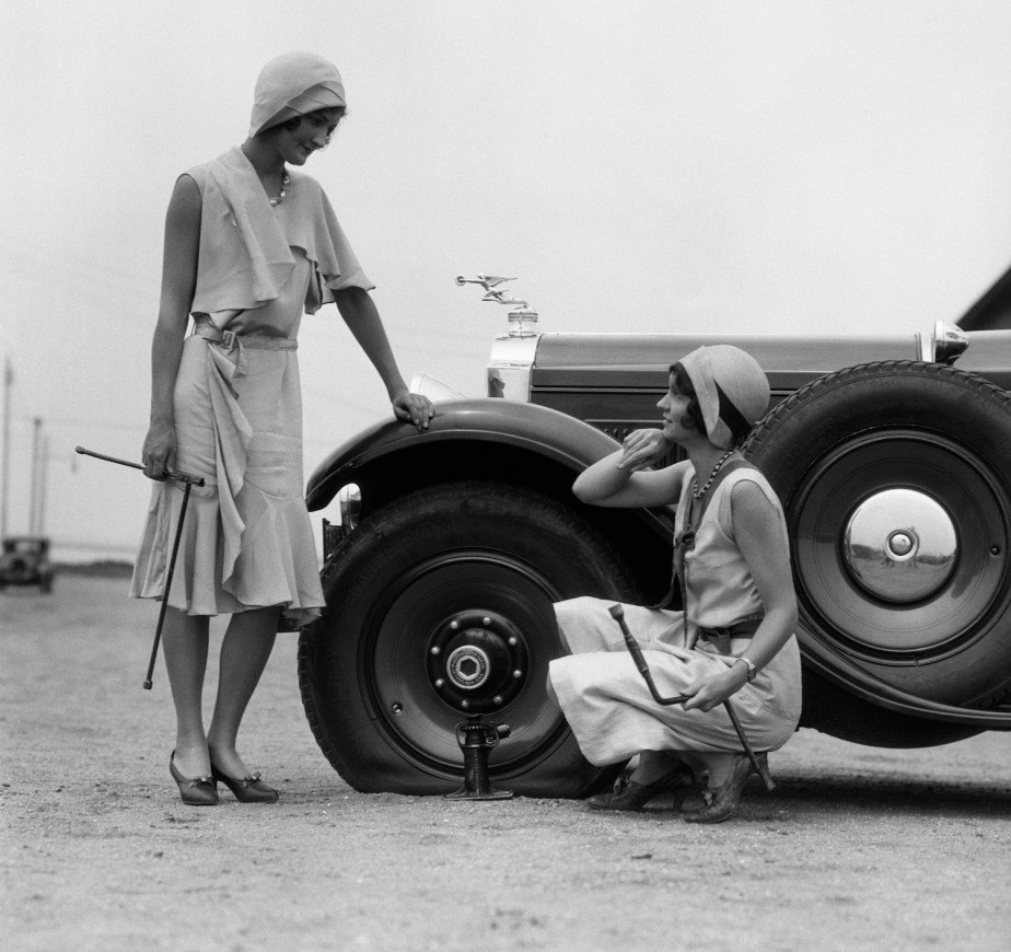 Two women pose while changing a Rolls-Royce tire in the 1930s.