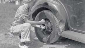 Black and white photo of a pioneering young female mechanic changing a tire in 1937.