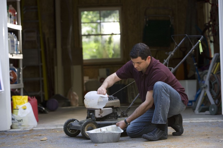 A person with the oil for lawn mower changing the oil.