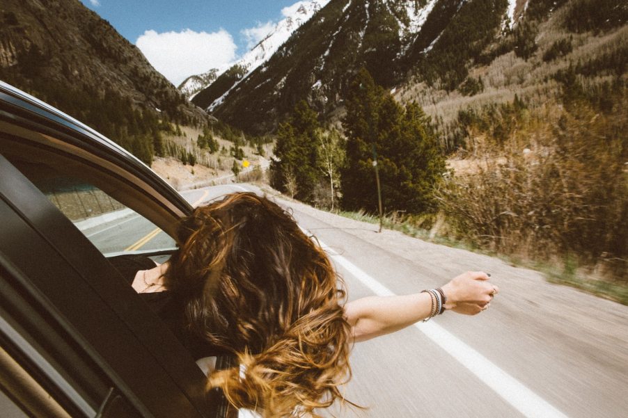 Woman hangs out the passenger window of a car navigating a mountain road.