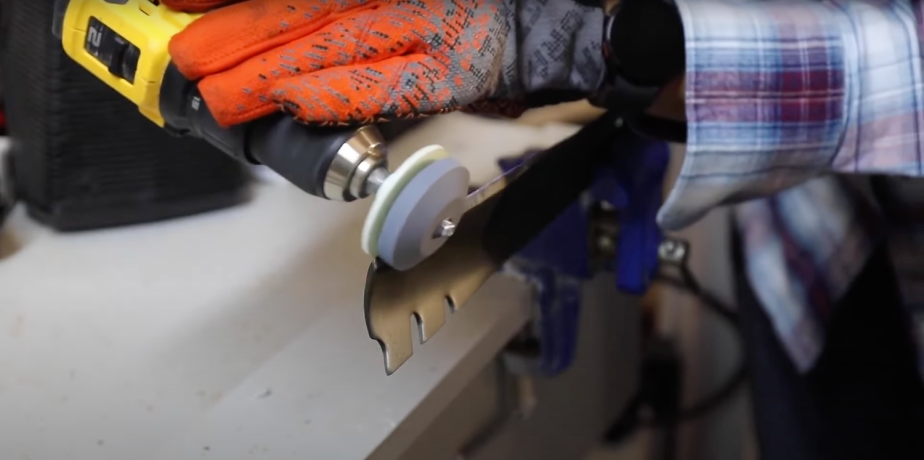 Lawn mower mechanic using a drill to sharpen a blade.