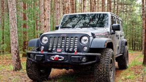 Modified Jeep Wrangler 4x4 with a winch parked in the woods.