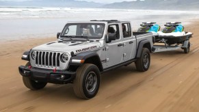 The 2022 Jeep Gladiator shows off its capability as a mid-size truck, it tows two watercraft on a beach.