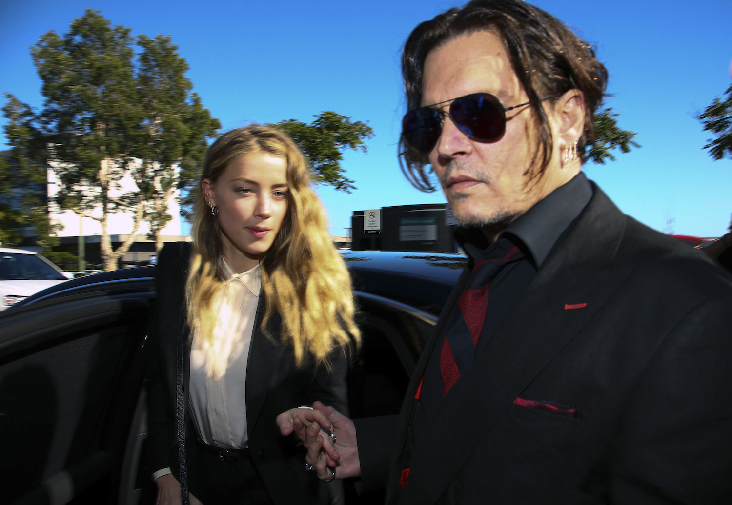 Johnny Depp and Amber Heard getting out of a black sedan in a sunny parking lot.