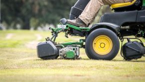 A riding lawn mower front end with someone riding on it.