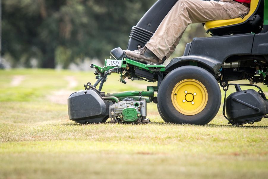 A riding lawn mower front end with someone riding on it.