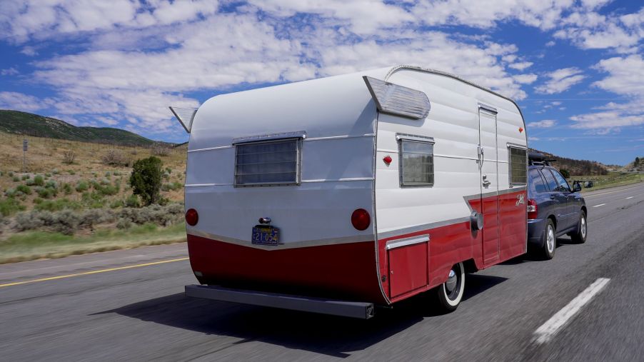 A red and white RV, possibly in need of DIY RV upgrades, being pulled by a truck.