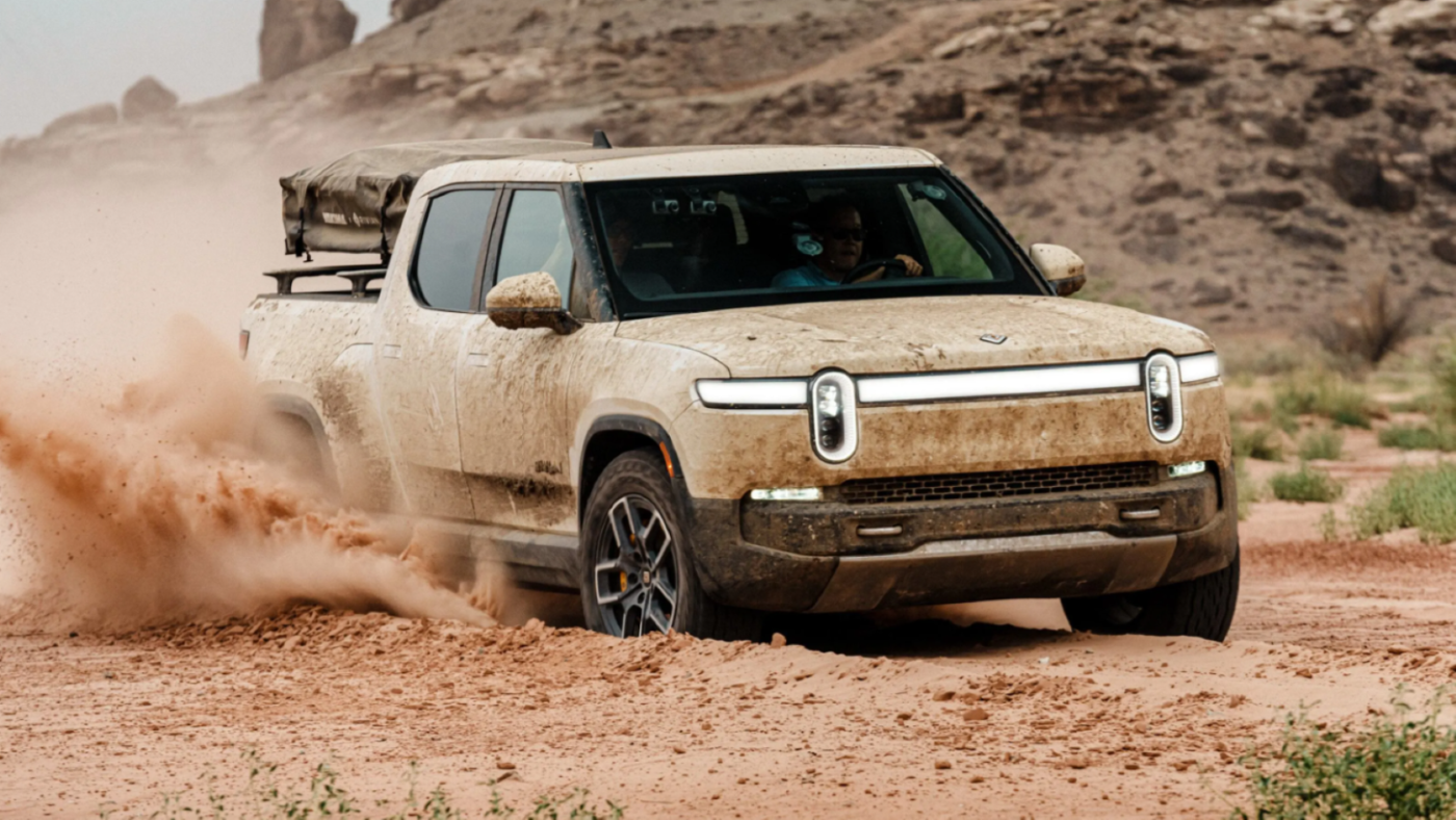 The Rivian R1T all-electric pickup truck model covered in dirt and grime while driving off-road in wet mud and earth