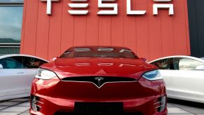 Tesla written in white on a red wall with red and white Teslas sitting in front of it.