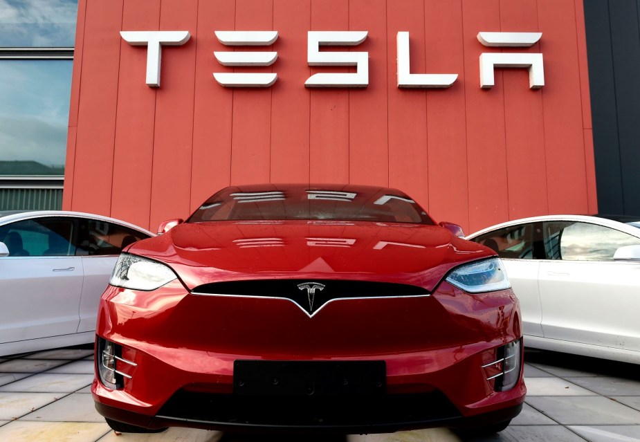 Tesla written in white on a red wall with red and white Teslas sitting in front of it. 