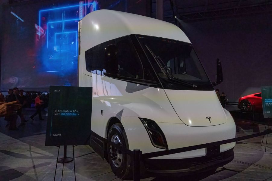 A white Tesla semi-truck parked in an indoor area with blue lights in the background.