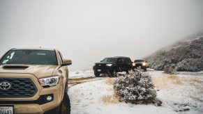 Convoy of Toyota Tacoma midsize pickup trucks driving through snow in the mountains.