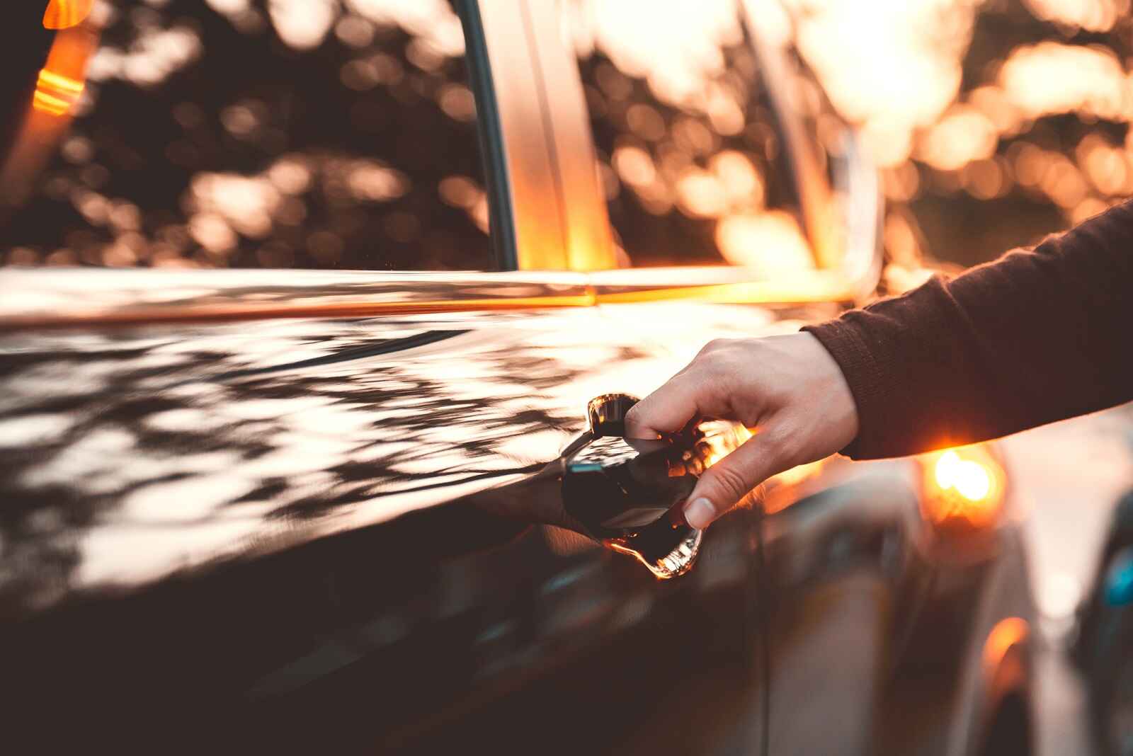 An arm is shown from right frame opening a black car door at dusk in close view