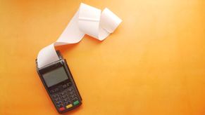 A black adding machine with a strip of black machine tape coming out, laying on an orange tape; calculating car financing rates is an important part of the buying process