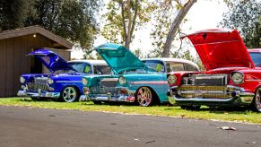 Three classic cars on a consignment lot: blue, teal, and red.