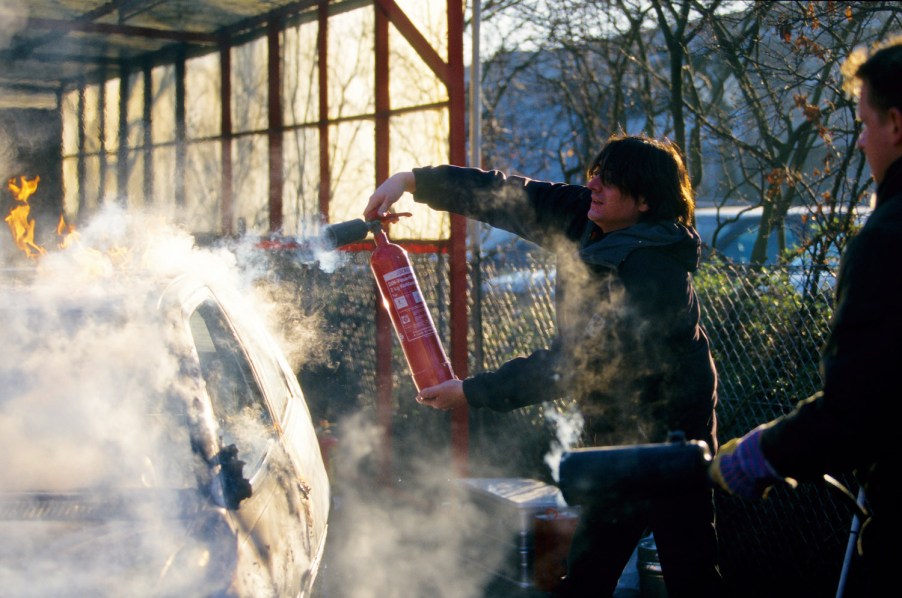 A man puts out a car fire with an extinguisher.