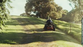 Man mowing grass along a fenceline with trees.