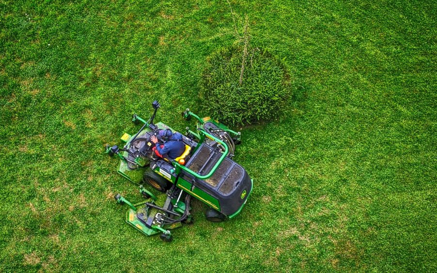 Birds-eye view of a green John Deer ride-on lawn mower in a field.