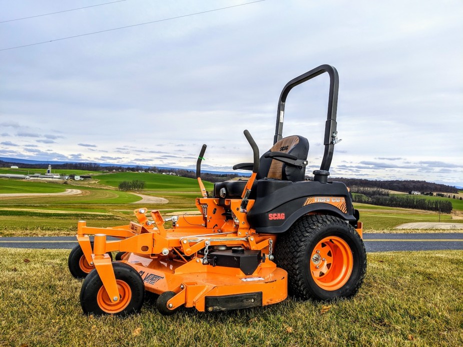 Orange ride-on lawn mower parked on a hill overlooking a town.