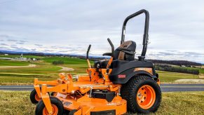 Orange, Scag riding lawn mower parked above a road and town.