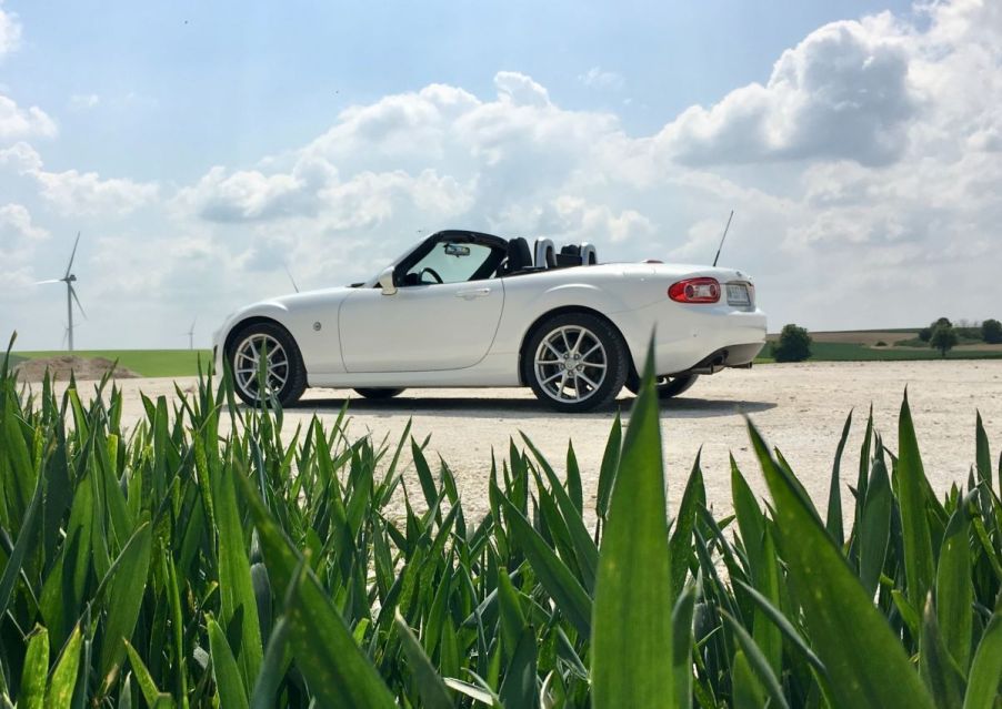 White Mazda Miata parked on a sunny road with bright green grass in front of the