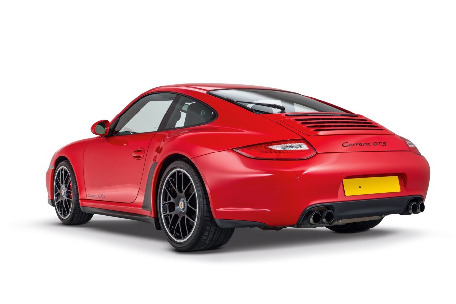 The rear 3/4 view of a red-and-black 2011 997 Porsche 911 Carrera GTS in a white studio