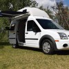 A white 2011 Ford Transit Connect XLT camper van in a field with its awning extended