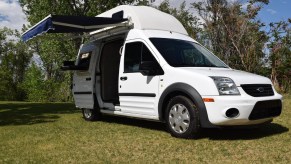 A white 2011 Ford Transit Connect XLT camper van in a field with its awning extended