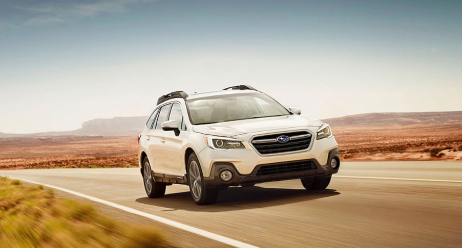 A white 2019 Subaru Outback midsize SUV is driving on the road.