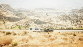 Nissan Titan XD medium duty pickup truck showing off its towing capacity by pulling a camper trailer down a rural road, mountains visible in the background.