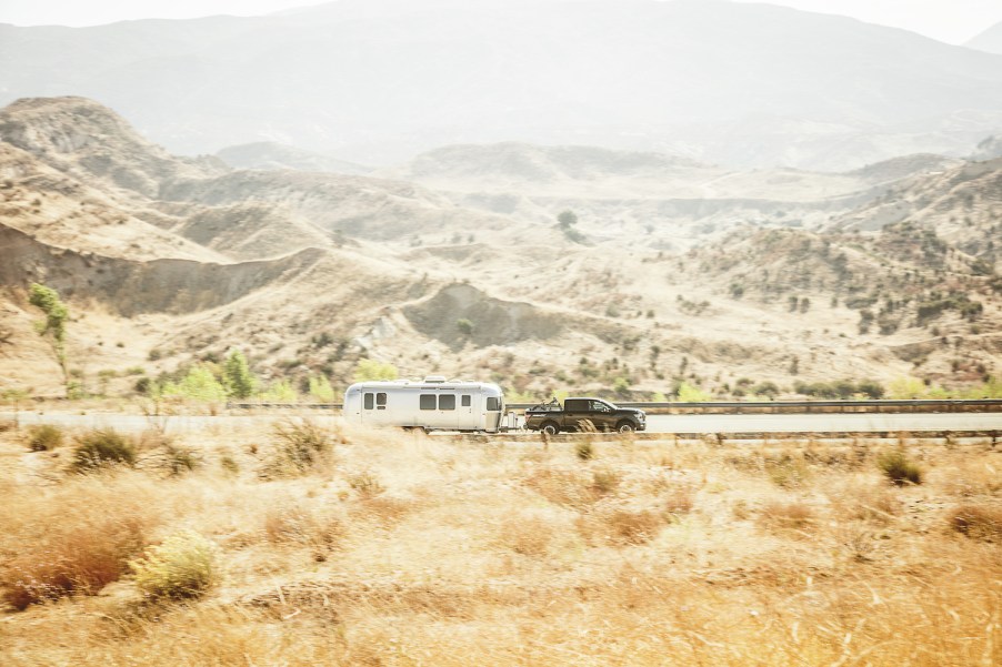 Nissan Titan XD medium duty pickup truck showing off its towing capacity by pulling a camper trailer down a rural road, mountains visible in the background.