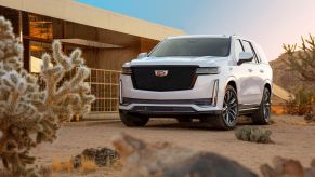 A white 2021 Cadillac Escalade full-size luxury SUV parked in the desert near a luxury home