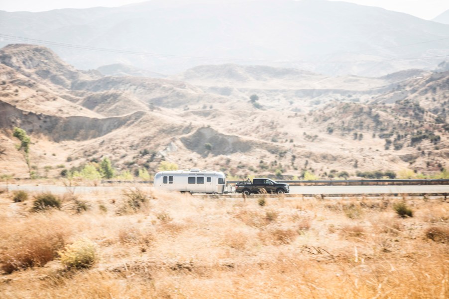 Distant Nissan Titan pickup truck towing a camper along a road, a mountain range visible behind it.