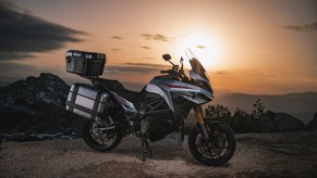 The side view of a gray-and-red 2022 Energica Experia with luggage on its center stand in the desert